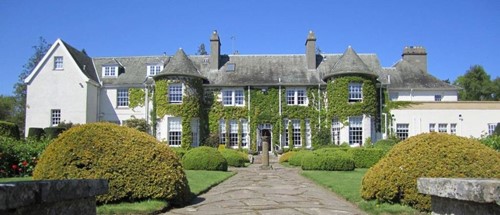 Front view of Rufflets St Andrews with green ivy and sculpted hedges under a bright blue sky.